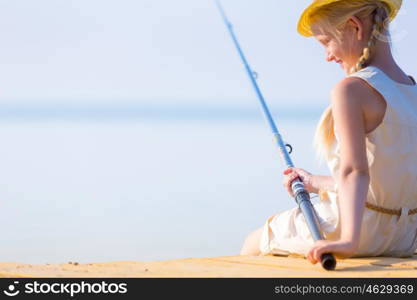 Girl in a dress and a hat with a fishing rod fishing from the pier