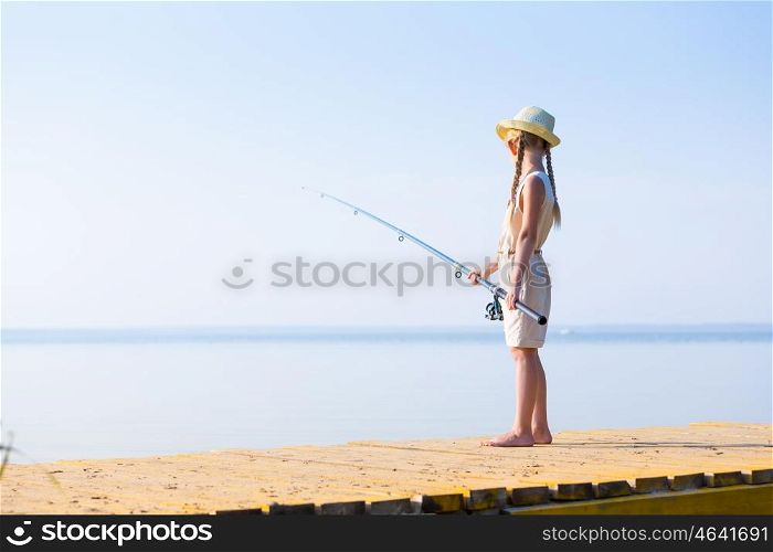 Girl in a dress and a hat with a fishing rod fishing from the pier
