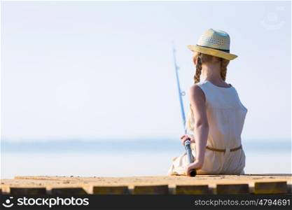 Girl in a dress and a hat with a fishing rod fishing from the pier