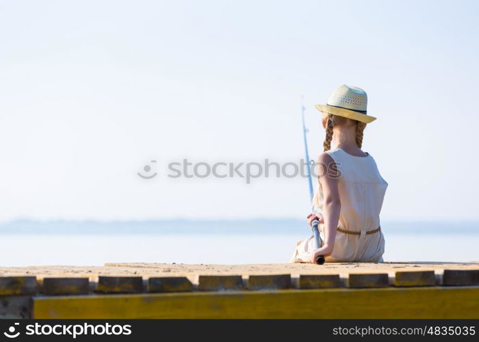 Girl in a dress and a hat with a fishing rod fishing from the pier