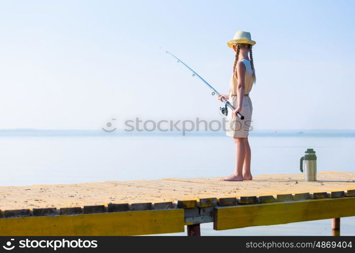 Girl in a dress and a hat with a fishing rod fishing from the pier