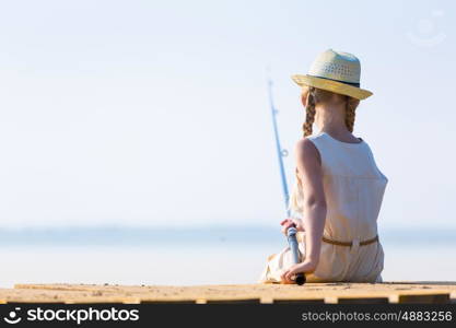 Girl in a dress and a hat with a fishing rod fishing from the pier