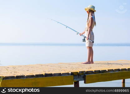 Girl in a dress and a hat with a fishing rod fishing from the pier