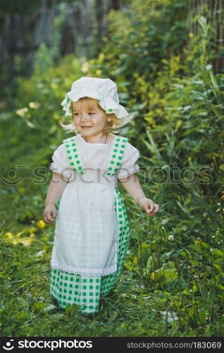 Girl in a dress in green peas in the garden.. Little girl in green and white dress walking in the garden 4657.