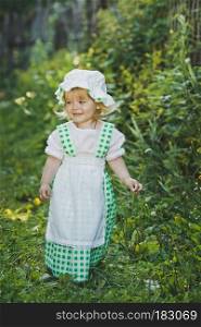 Girl in a dress in green peas in the garden.. Little girl in green and white dress walking in the garden 4657.