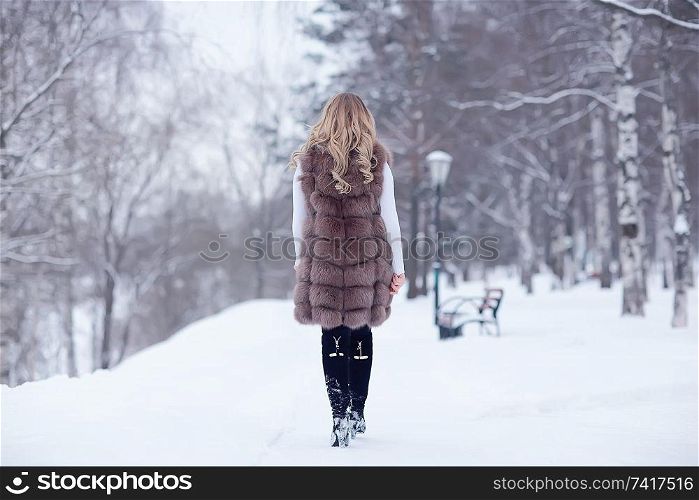 girl in a fur vest walks in the winter outside / adult young model in winter clothes fur