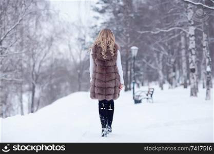 girl in a fur vest walks in the winter outside / adult young model in winter clothes fur