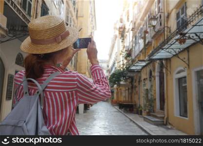 girl in a hat walks on the street of the ancient Greek city and takes pictures on camera. Corfu Island in Greece,