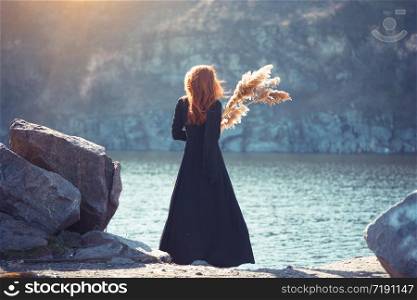 girl in a long black dress stands on the shore of the fjord