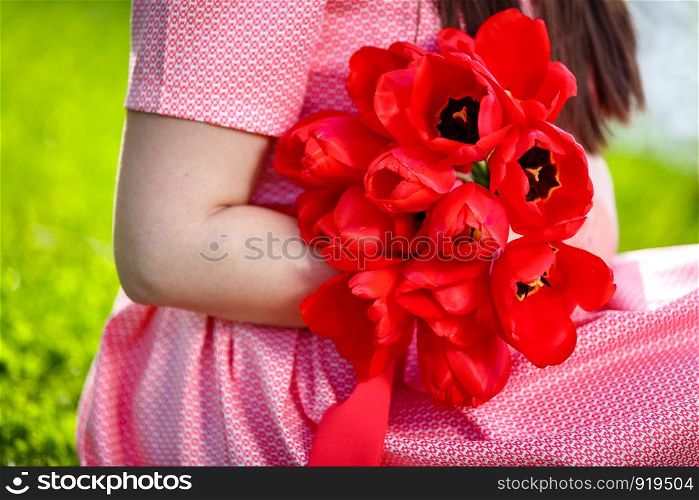 girl in a pink dress with spring red flowers in her hands. girl in a pink dress with spring red flowers in her hands. side view back background