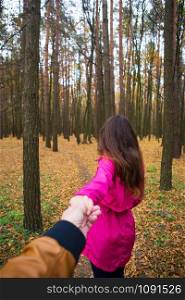 girl in a pink raincoat holds her boyfriend&rsquo;s hand in the autumn forest.. girl in a pink raincoat holds her boyfriend&rsquo;s hand in the autumn forest