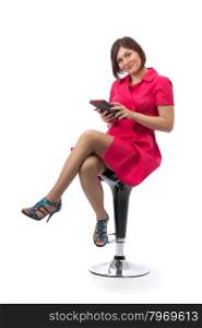 Girl in a red dress with a Tablet PC in the hands on a bar chair in the studio. Isolate on white.