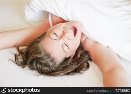 girl in a white bed yawns and stretches in the morning