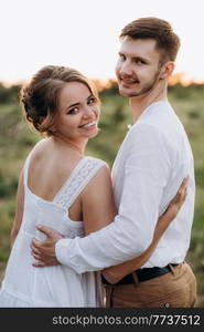 girl in a white sundress and a guy in a white shirt on a walk at sunset with a bouquet in a village outside the city