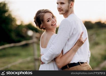 girl in a white sundress and a guy in a white shirt on a walk at sunset with a bouquet in a village outside the city