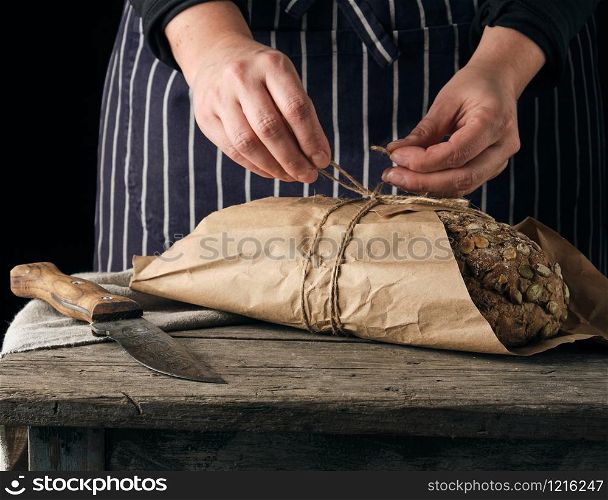 girl in black clothes wraps a whole baked loaf of bread in brown kraft paper and ties
