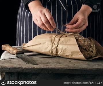 girl in black clothes wraps a whole baked loaf of bread in brown kraft paper and ties