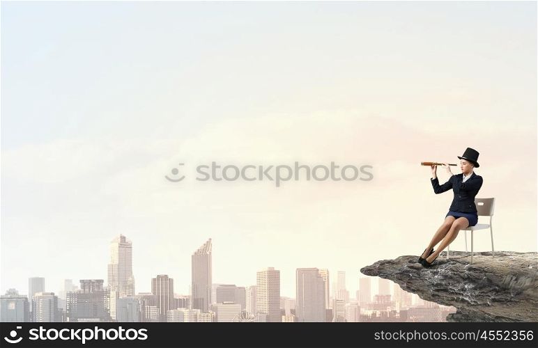 Girl in black cylinder. Pretty girl wearing retro hat siting on chair and looking in spyglass