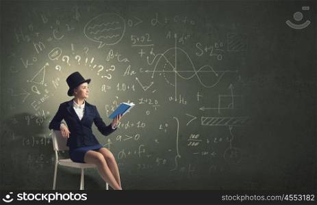 Girl in black cylinder. Pretty girl wearing retro hat siting on chair with book in hands
