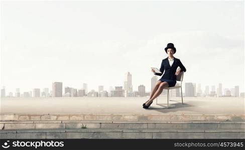 Girl in black cylinder. Pretty girl wearing retro hat siting on chair with tablet in hand