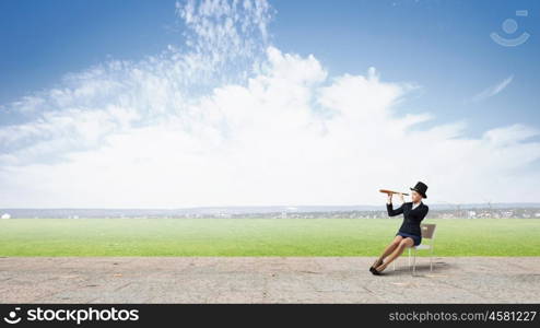 Girl in black cylinder. Pretty girl wearing retro hat siting on chair and looking in spyglass