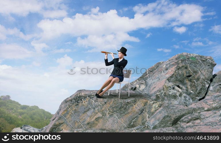 Girl in black cylinder. Pretty girl wearing retro hat siting on chair and looking in spyglass