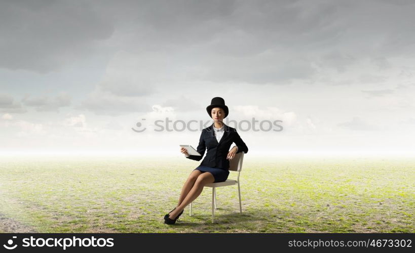 Girl in black cylinder. Pretty girl wearing retro hat siting on chair with tablet in hand