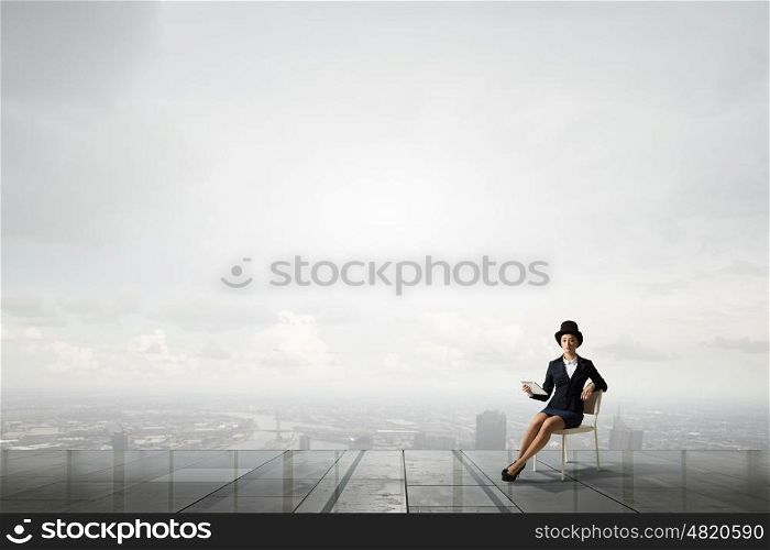 Girl in black cylinder. Pretty girl wearing retro hat siting on chair with tablet in hand