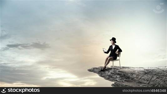 Girl in black cylinder. Pretty girl wearing retro hat siting on chair with alarm clock in hand