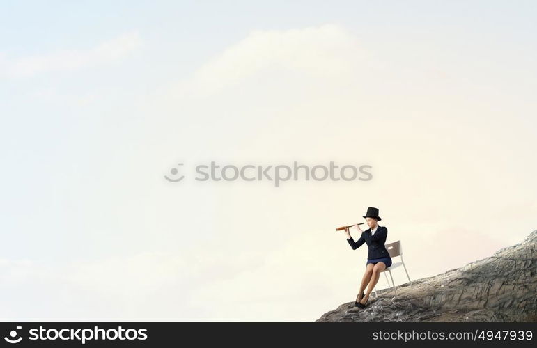 Girl in black cylinder. Pretty girl wearing retro hat siting on chair and looking in spyglass