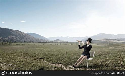 Girl in black cylinder. Pretty girl wearing retro hat siting on chair and looking in spyglass