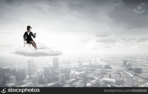 Girl in black cylinder. Pretty girl wearing retro hat siting on chair with alarm clock in hand