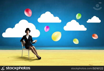 Girl in black cylinder. Pretty girl wearing retro hat siting on chair with tablet in hand