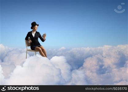 Girl in black cylinder. Pretty girl wearing retro hat siting on chair with clock in hand