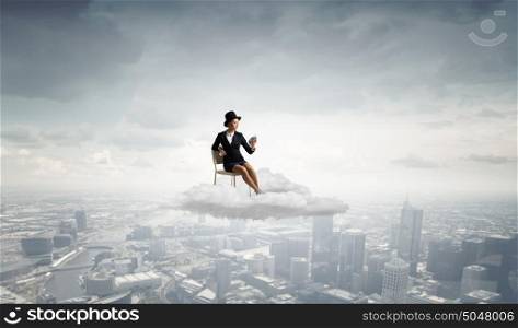 Girl in black cylinder. Pretty girl wearing retro hat siting on chair with alarm clock in hand