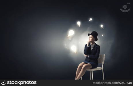 Girl in black cylinder. Pretty girl wearing retro hat siting on chair