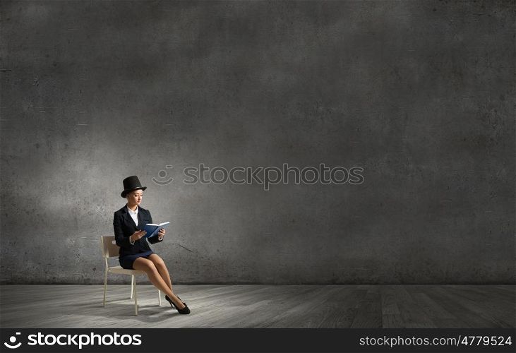Girl in black cylinder. Pretty girl wearing retro hat sitting on chair with book in hands