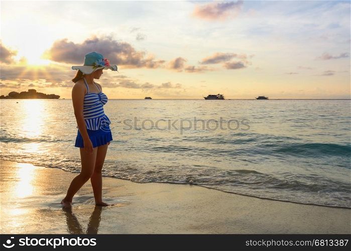 Girl in blue swimsuit walking on beach with happy and beautiful sky above the sea during sunrise at Honeymoon Bay, Koh Miang Islands, Similan National Park, Phang Nga, Thailand