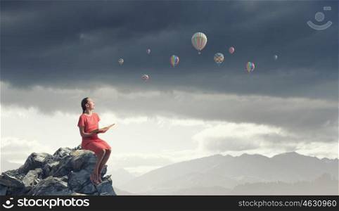 Girl in dress read book. Young attractive woman sitting on rock top and reading book