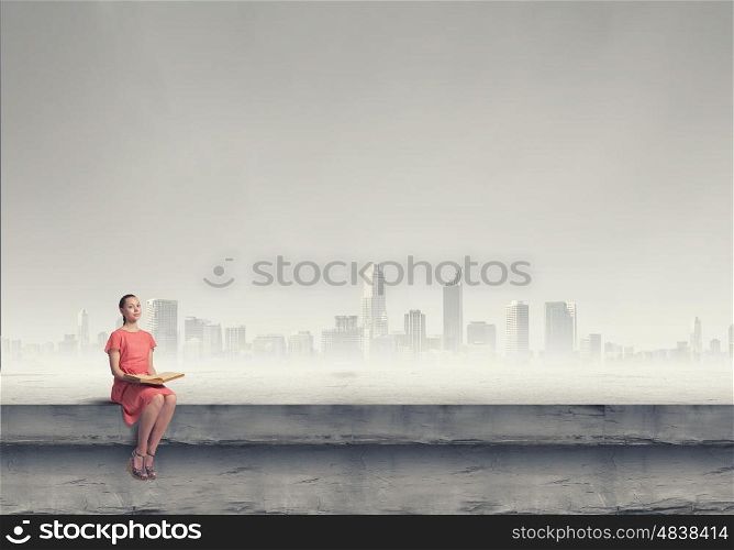 Girl in dress read book. Young attractive woman sitting on top of building and reading book