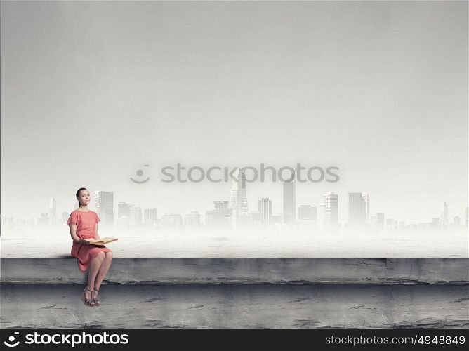 Girl in dress read book. Young attractive woman sitting on top of building and reading book