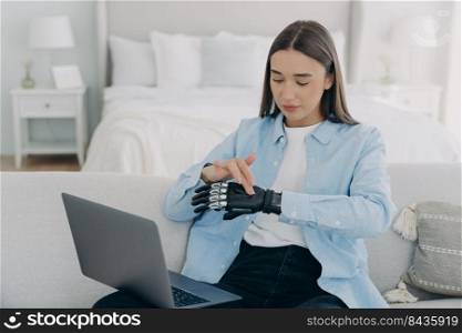 Girl in front of pc is setting bionic prosthesis. Young european woman is adjusting artificial hand. Attractive handicapped woman is working at home. Modern bionic prosthesis.. Girl in front of pc is setting bionic prosthesis. Young european woman is adjusting artificial hand.