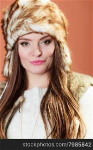 Girl in fur cap. Portrait of fashionable pretty woman in fur winter cap hat on orange background in studio.
