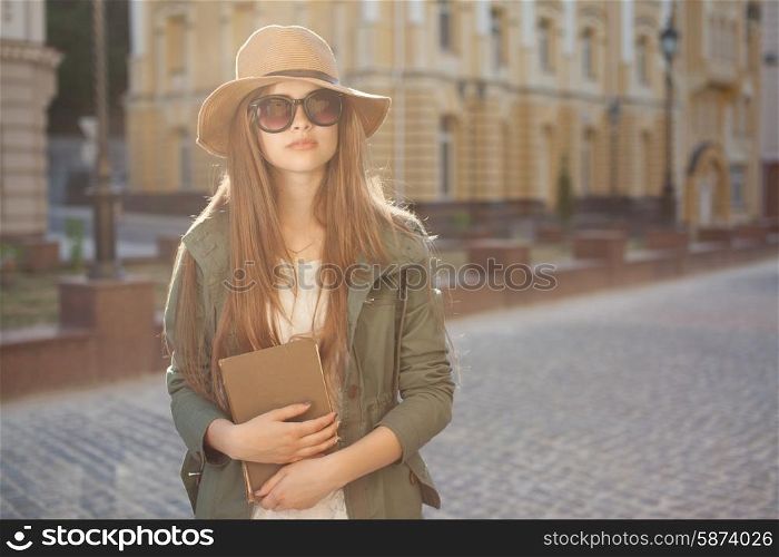 girl in hat and glasses holding book outdoors