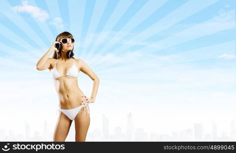 Girl in headphones. Young attractive girl in bikini wearing headphones touching media icon