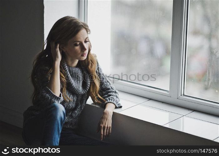 Girl in home clothes sitting at the window.. The girl is sitting by the large window 6998.