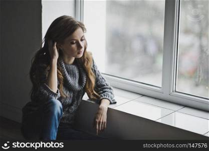 Girl in home clothes sitting at the window.. The girl is sitting by the large window 6998.