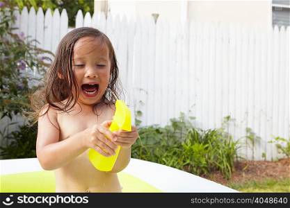 Girl in inflatable pool, excited over toy