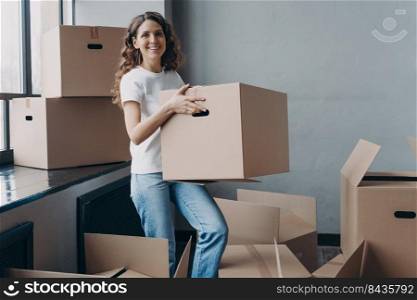 Girl in jeans and white t-shirt is carrying cardboard box. Happy attractive european woman packing things to move. Packed boxes on the floor. Relocation and moving to new apartment concept.. Girl in jeans and white t-shirt is carrying cardboard box. Happy woman packing things to move.