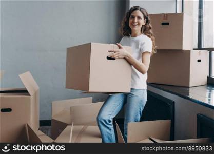 Girl in jeans and white t-shirt is carrying cardboard box. Happy attractive european woman packing things to move. Packed boxes on the floor. Relocation and moving to new apartment concept.. Girl in jeans and white t-shirt is carrying cardboard box. Happy woman packing things to move.
